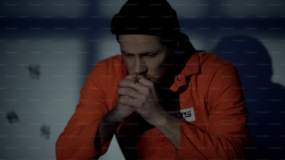Un homme emprisonné européen tenant une croix d’argent et priant dans une cellule se sentant coupable
