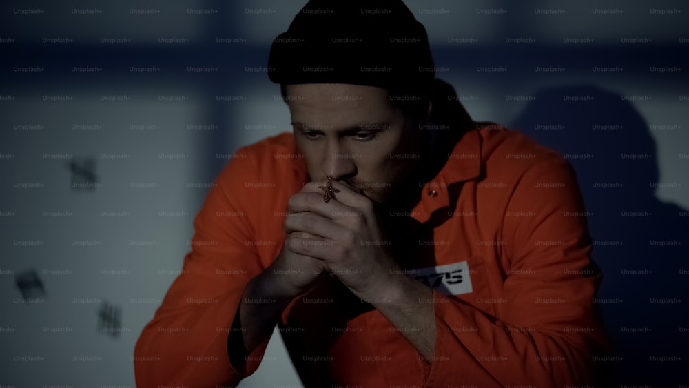 European imprisoned male holding silver cross and praying in cell feeling guilty