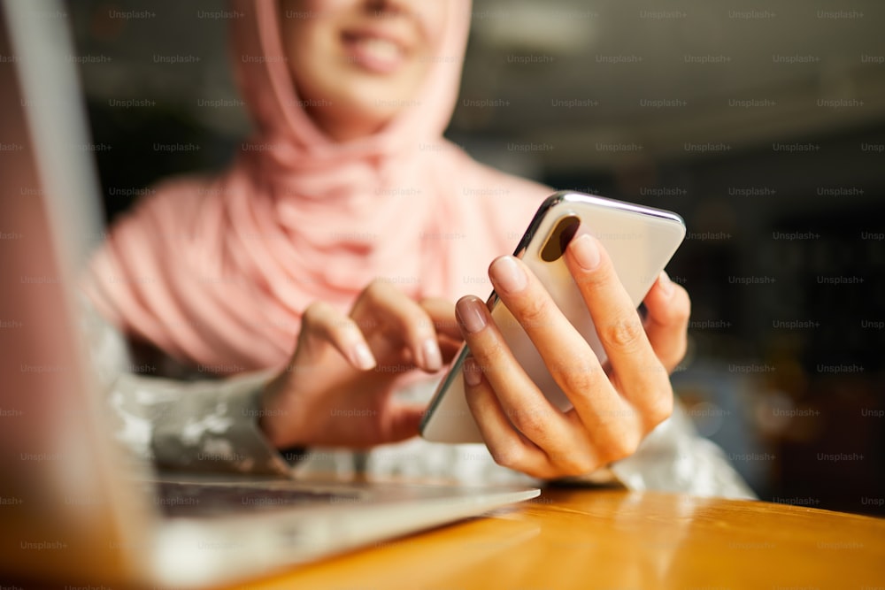 Manicured hands of woman in hijab sending text message
