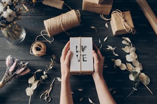 High angle view of unrecognizable woman holding gift made with love, twine, kraft paper and dried flowers on table