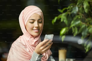 Portrait of young beautiful Muslim woman smiling when reading text message on her smartphone