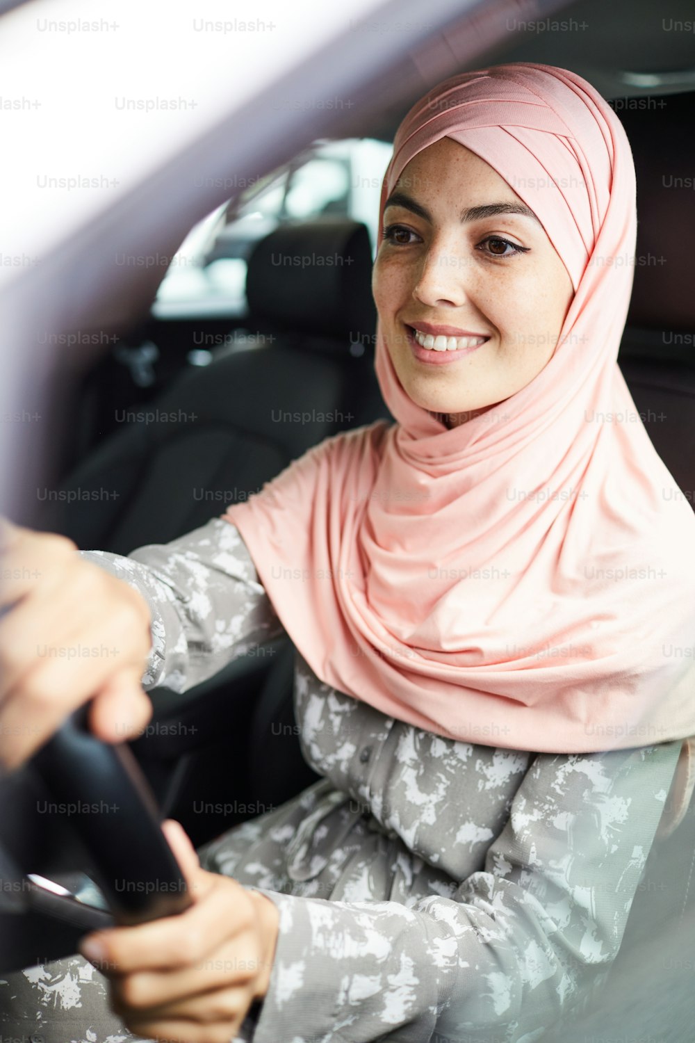 Happy confident young Arabian woman in pink hijab sitting at steering wheel and driving car