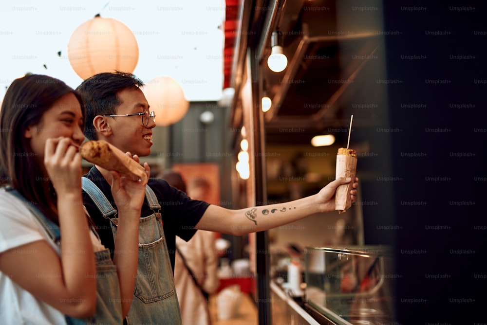 Concepto de comida rápida. Feliz amado joven asiático y mujer comprando maíz dulce a la parrilla en un café de la calle