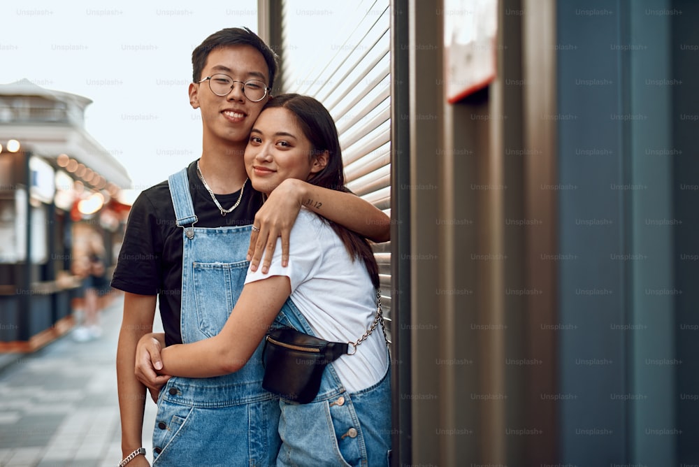 Liebes- und Date-Konzept. Junge glückliche asiatische Liebhaber Mann und Frau umarmen sich zärtlich, während sie in der Nähe des Straßencafés bleiben