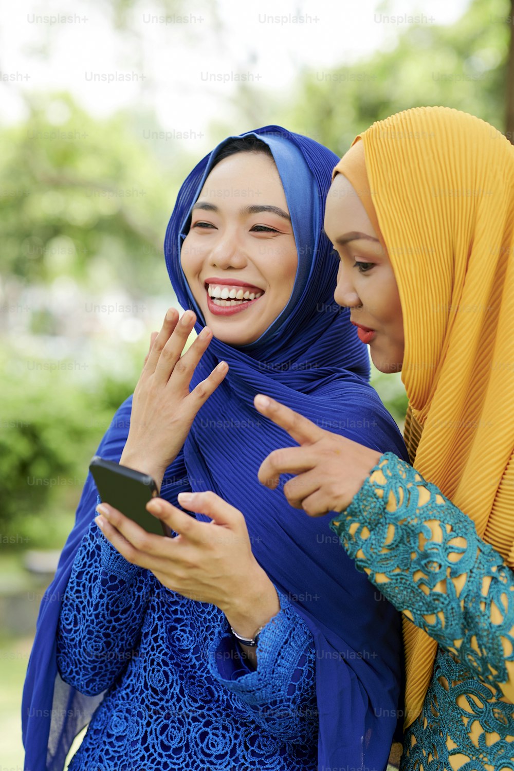 Two pretty muslim women laughing when reading text message from their friend on smartphone screen