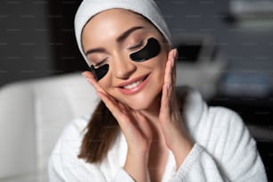 Charming lady with masks under her lower eyelids putting hands on her cheeks