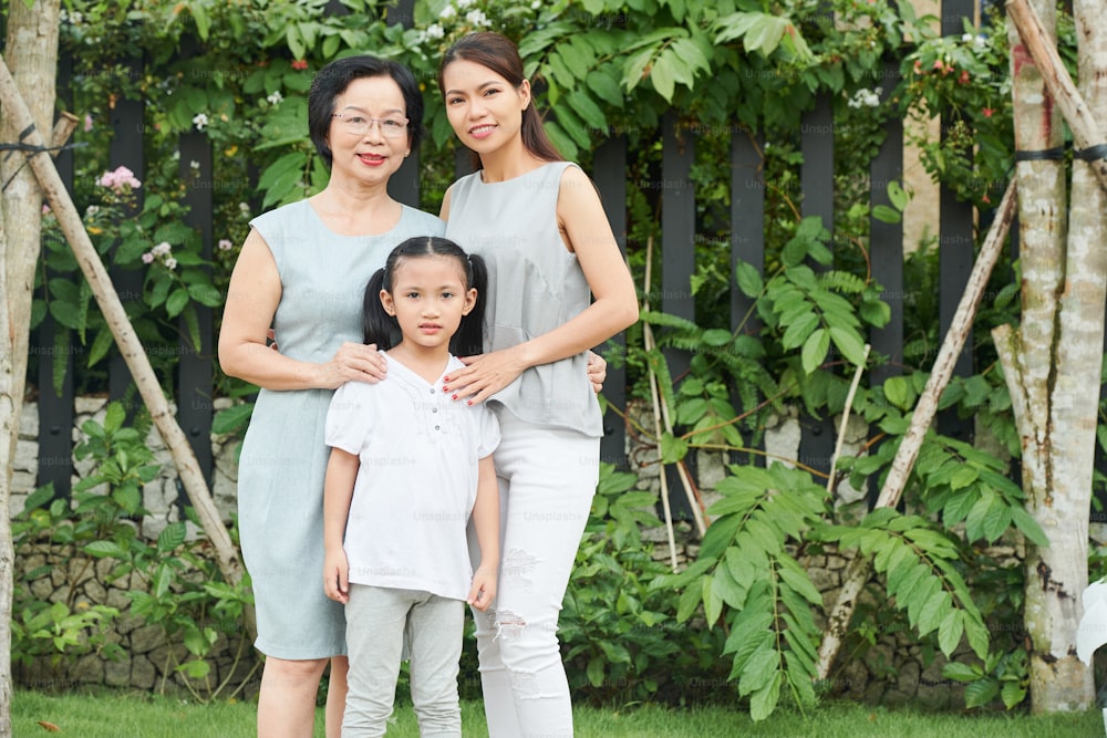 아시아계 가족 세대의 초상화는 야외에 서서 푸른 나무들을 배경으로 웃고 있다