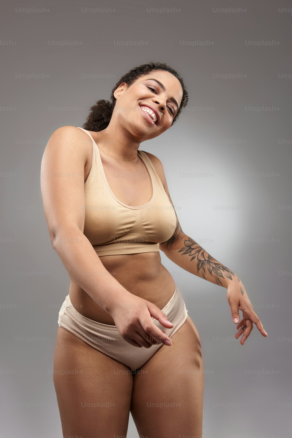 Joyful young pretty lady with tattoo on arm wearing light underwear. Overweight concept