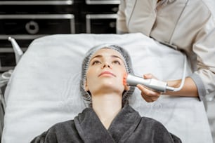 고급 미용실에서 여성에게 산소 메조테라피를 하는 여성 미용사. 전문적인 얼굴 치료의 개념