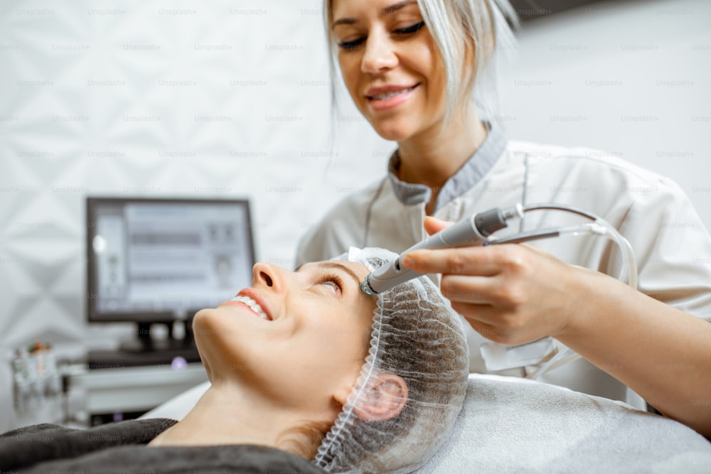 Cosmetologist making vacuum hydro peeling on the forehead region to a woman at the luxury beauty salon. Concept of a professional facial treatment