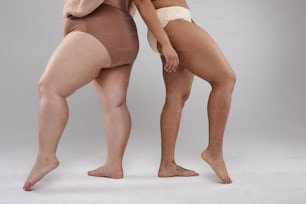 Cropped photo of Caucasian woman and Afro American lady demonstrating their buttocks