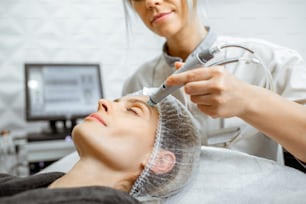 Cosmetologist making vacuum hydro peeling on the forehead region to a woman at the luxury beauty salon. Concept of a professional facial treatment