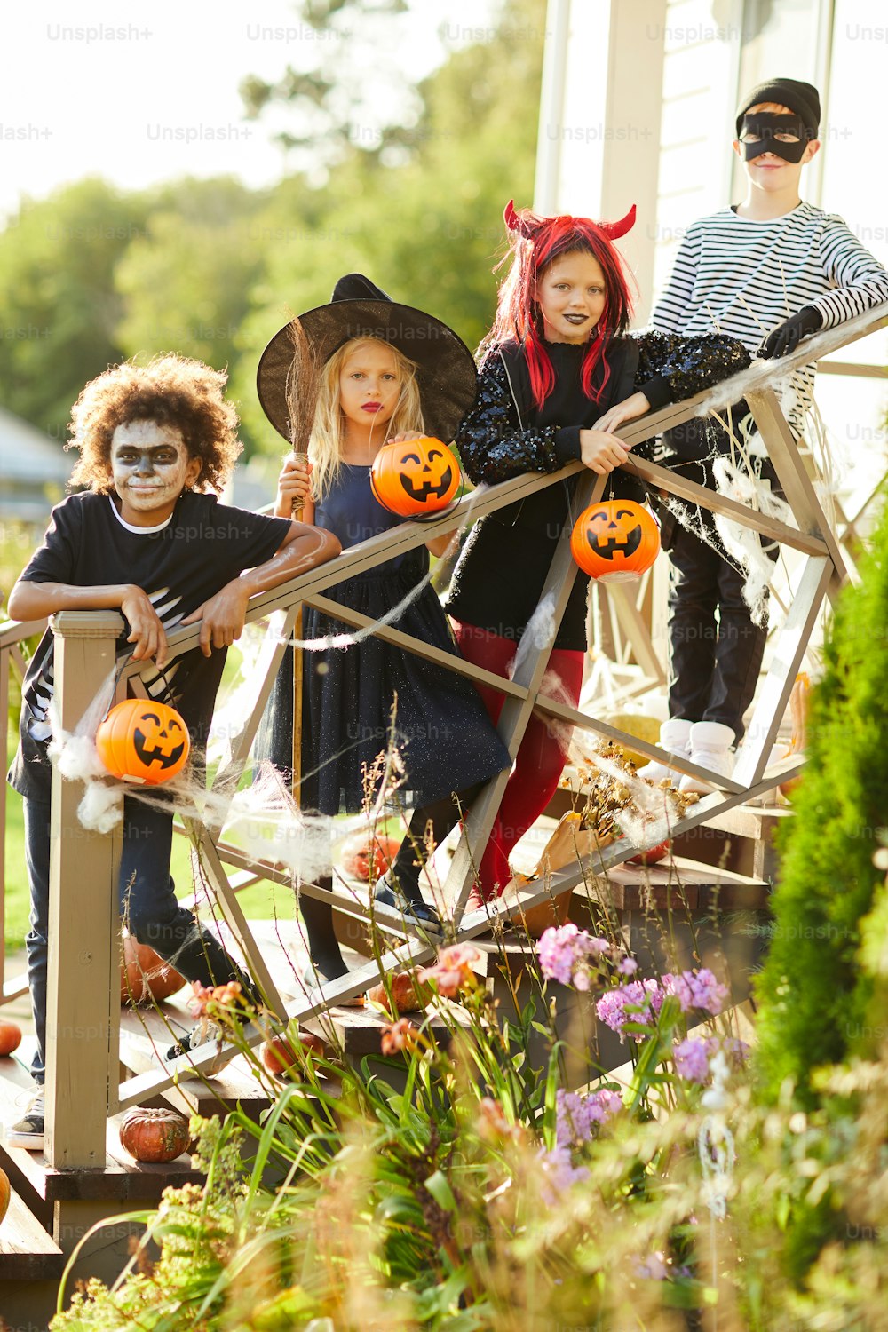 Gruppo multietnico di bambini che indossano costumi di Halloween in piedi sulle scale della casa decorata mentre si godono dolcetto o scherzetto insieme