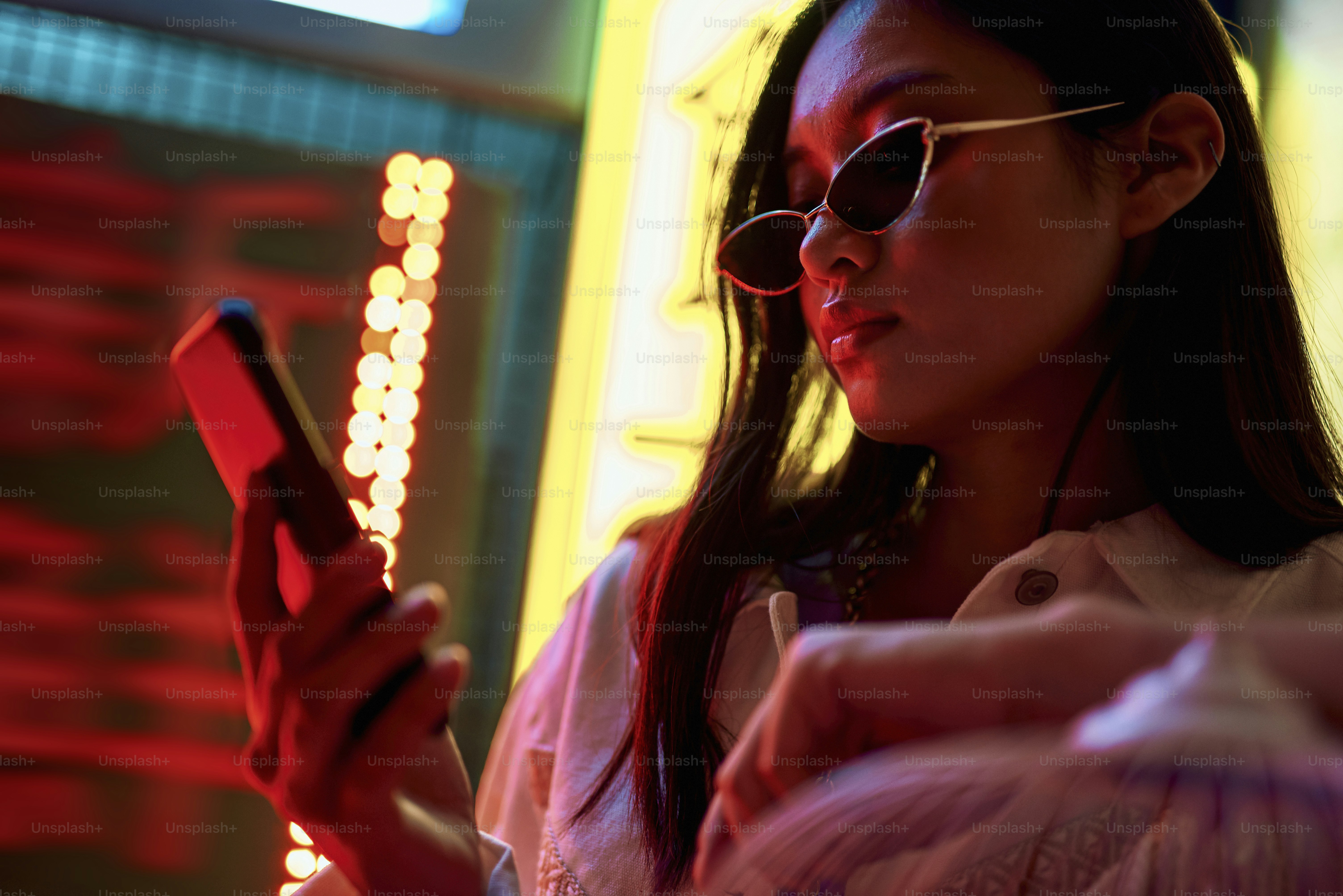 Oriental street culture. Young pretty stylish asian woman in cat eye sunglasses looking at mobile phone