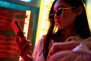 Oriental street culture. Young pretty stylish asian woman in cat eye sunglasses looking at mobile phone