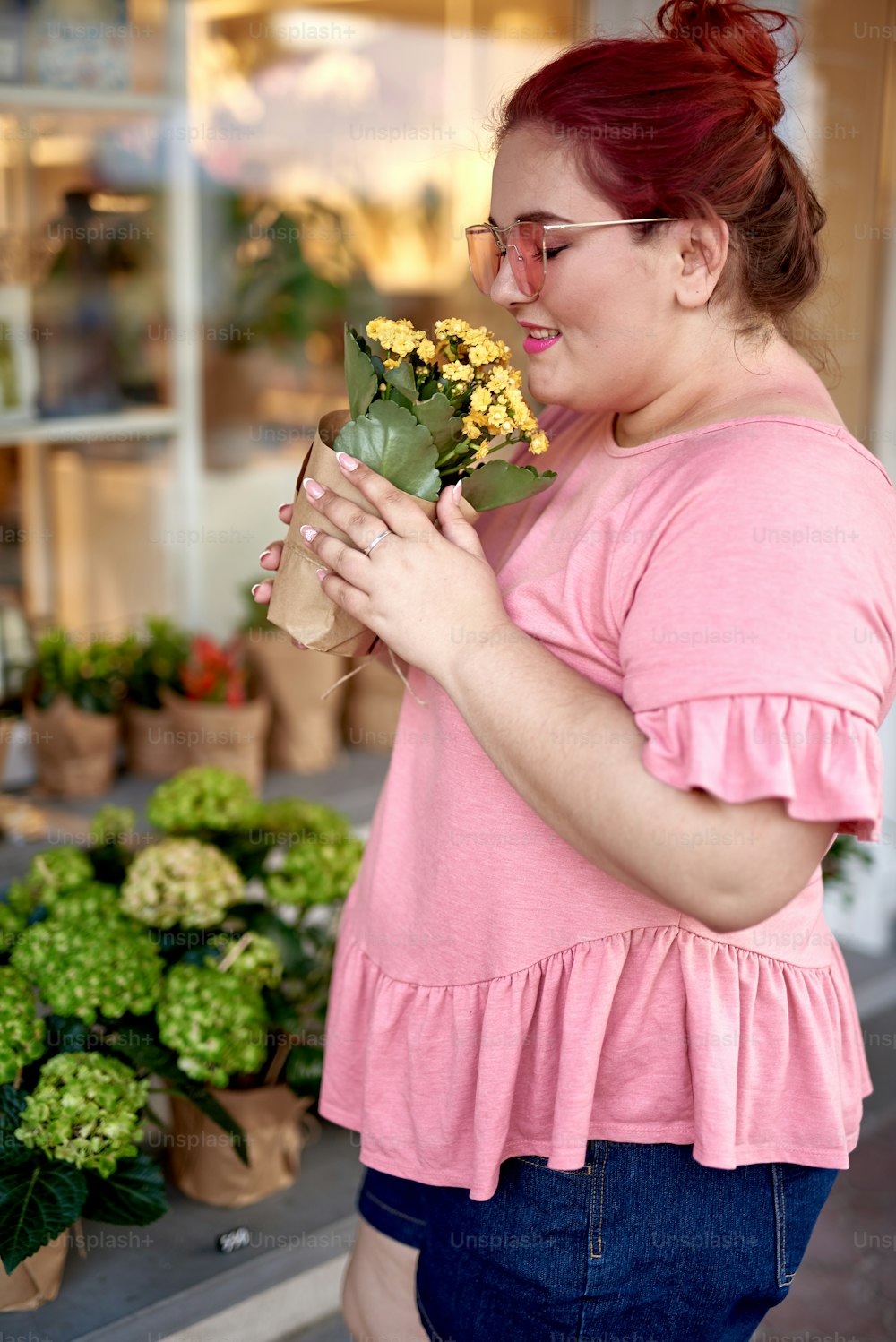 Cheerful fat and young woman smelling flower pot with blooming plant
