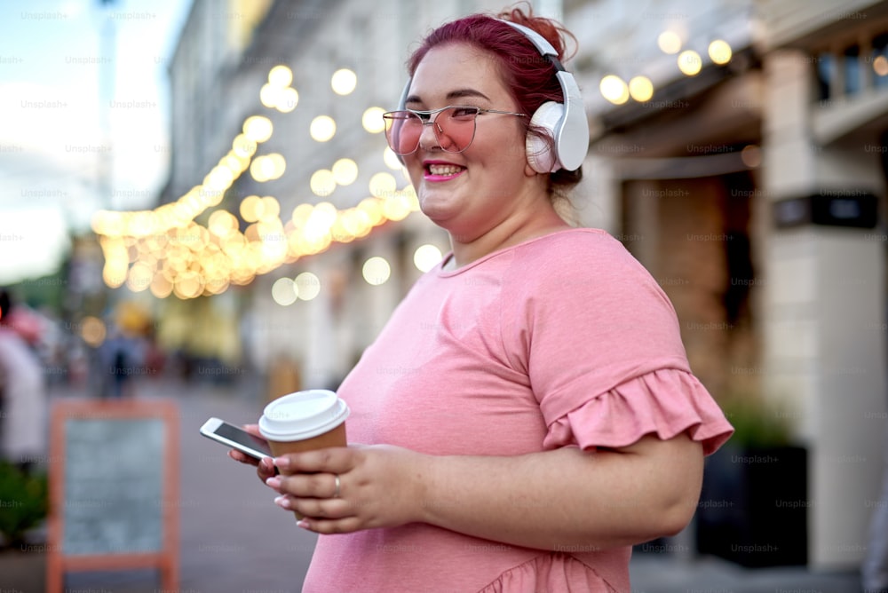 Happy fat woman listening music and holding smartphone on the street