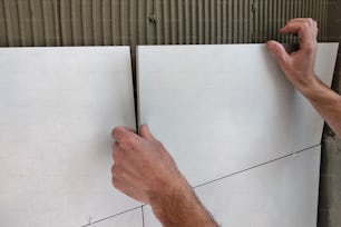 Worker hands putting ceramic tiles on the wall.