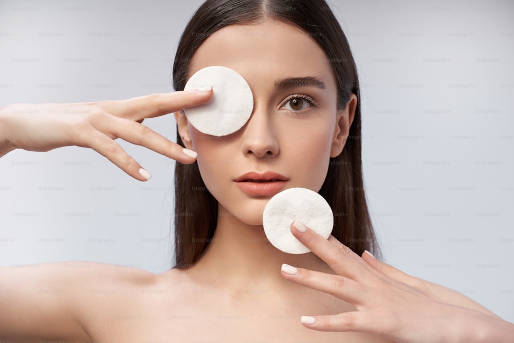 Cropped portrait of young lady looking at camera while holding two cosmetic cotton discs