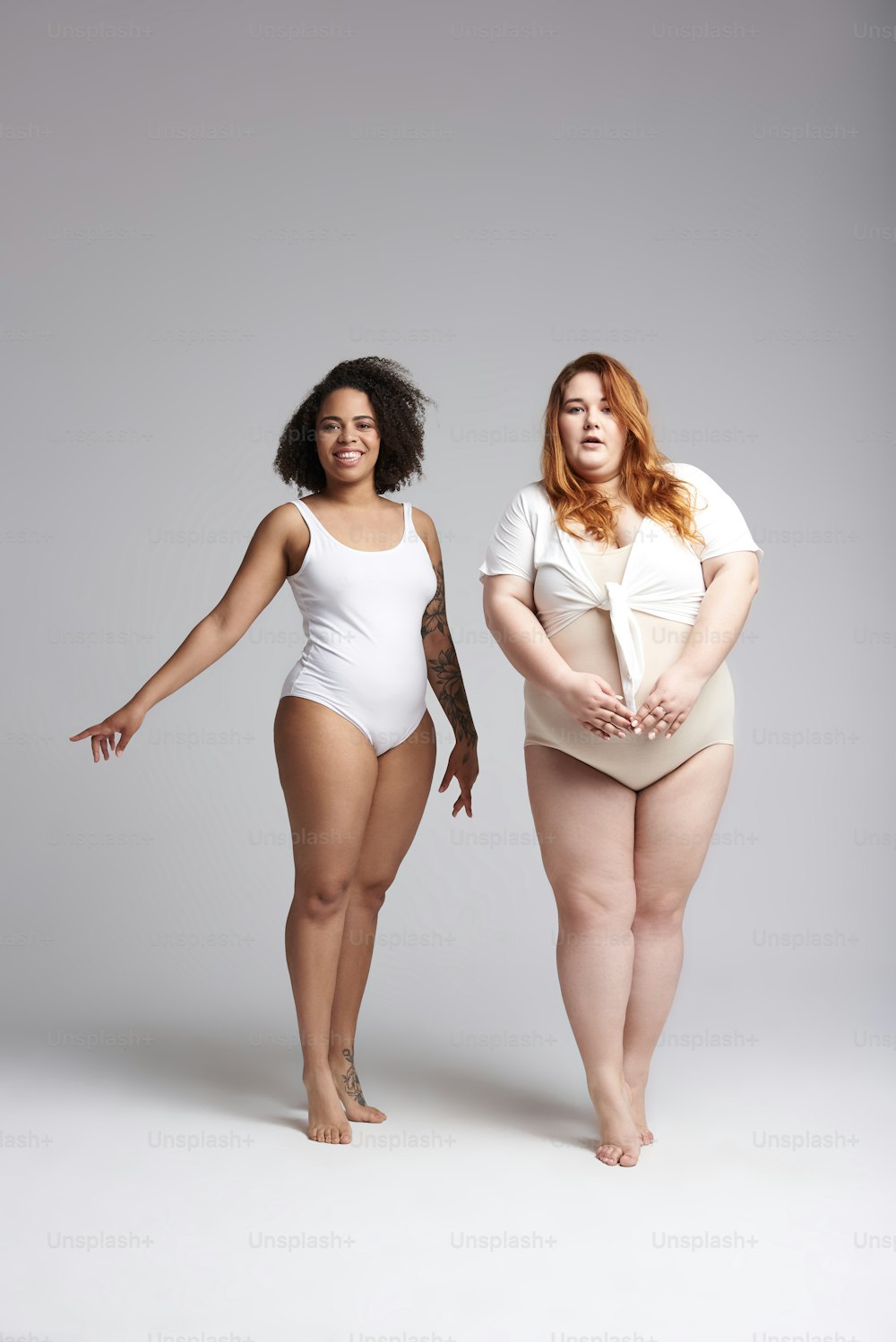 Mujer caucásica gorda feliz y mujer afroamericana mirando a la cámara mientras usa trajes de baño blancos