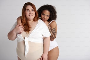 Dama afroamericana con tatuaje en el brazo abrazando a su amiga obesa caucásica