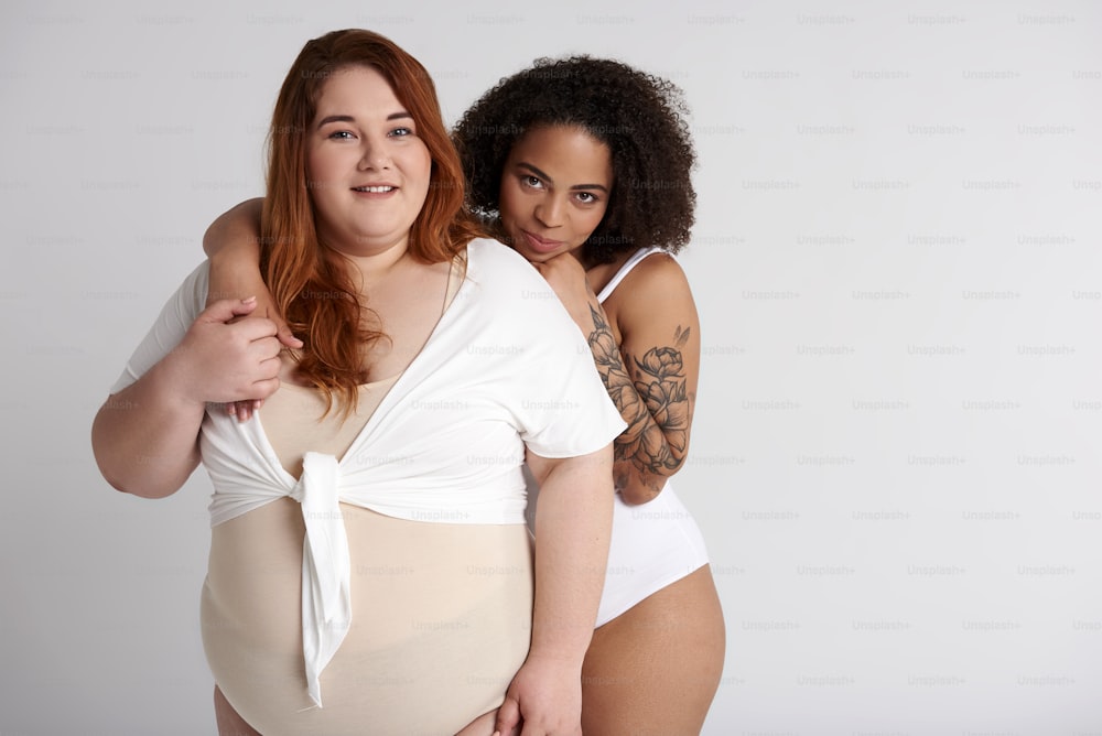 Afro American lady with tattoo on arm hugging her obese Caucasian female friend