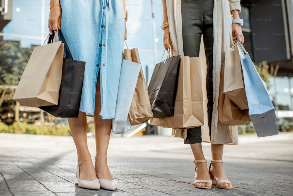 야외에서 쇼핑백을 들고 있는 여성들, 여성들의 다리와 가방을 가까이서 볼 수 있다