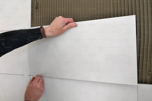 Worker hands putting ceramic tiles on the wall.