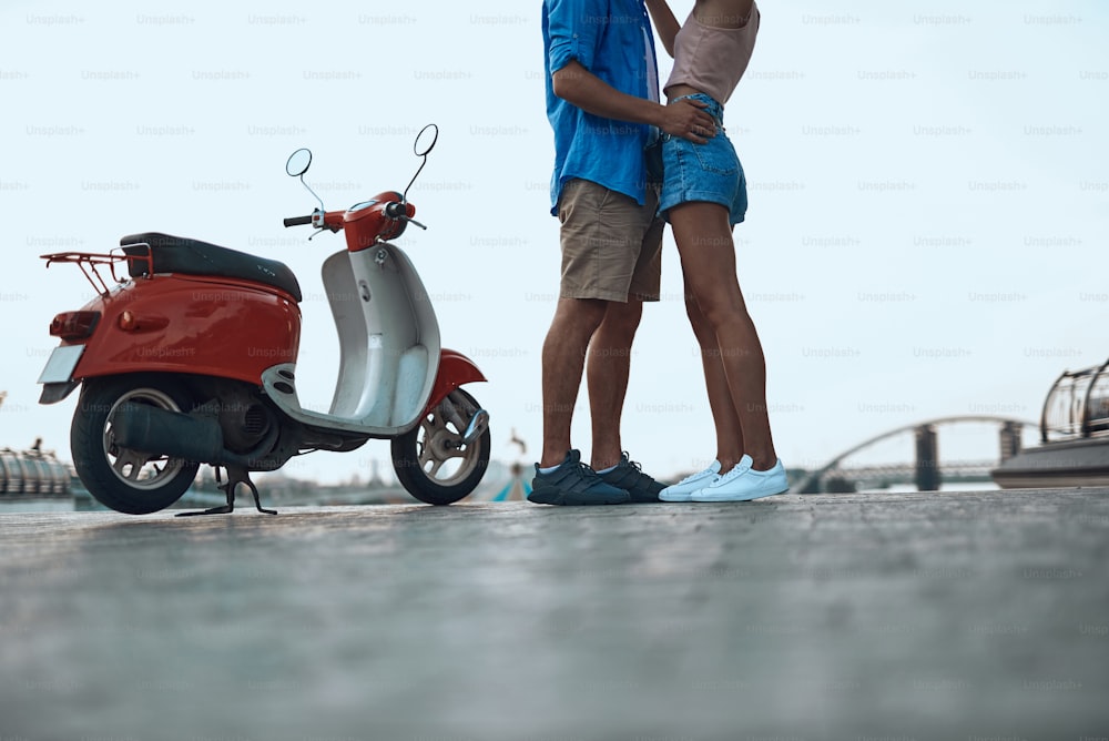 Moto moderna na rua. Jovem homem e mulher em shorts e tênis em pé perto
