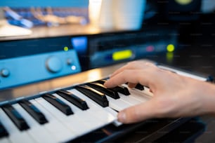 Hand des Pianisten, der eine der Tasten der Klaviertastatur drückt, während er Musik in einem zeitgenössischen Studio aufnimmt