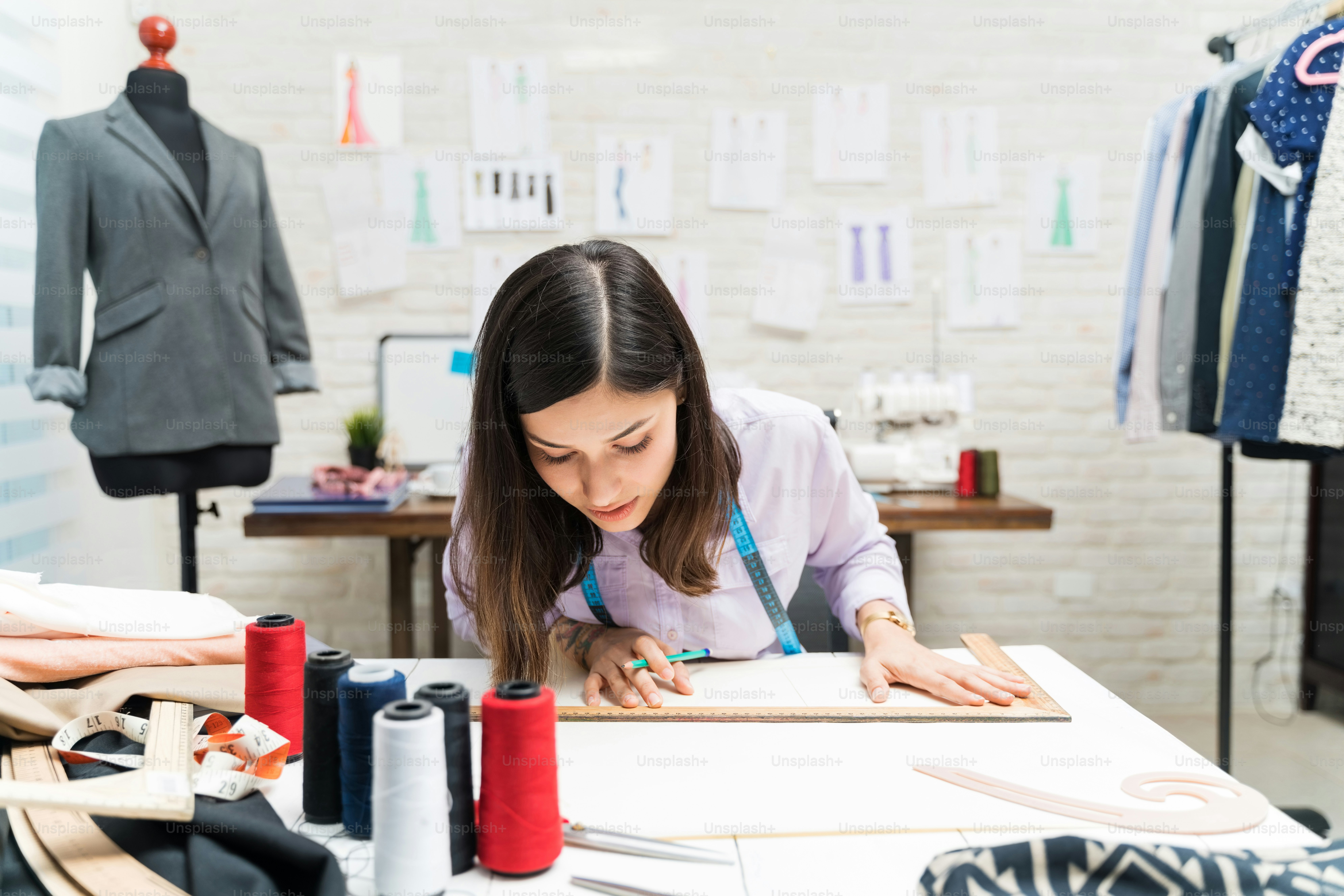 Beautiful female fashion designer drawing patterns on workbench while sitting in clothing studio