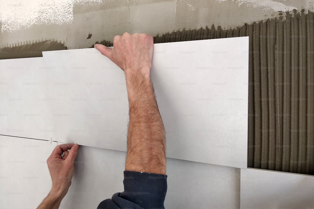 Worker hands putting ceramic tiles on the wall.