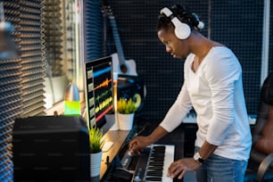 Selbstbewusster junger Musiker mit Kopfhörern, der gemischte Klänge über Kopfhörer hört, während er im Studio neue Musik macht