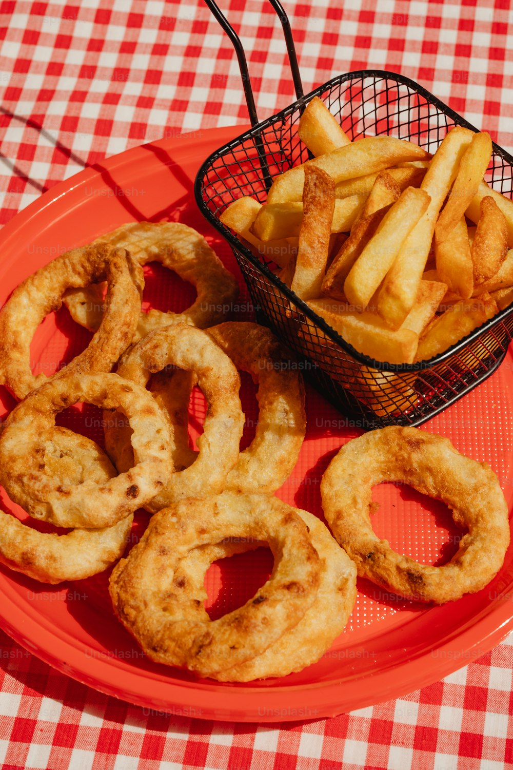 um prato vermelho coberto com anéis de cebola ao lado de uma cesta de batatas fritas