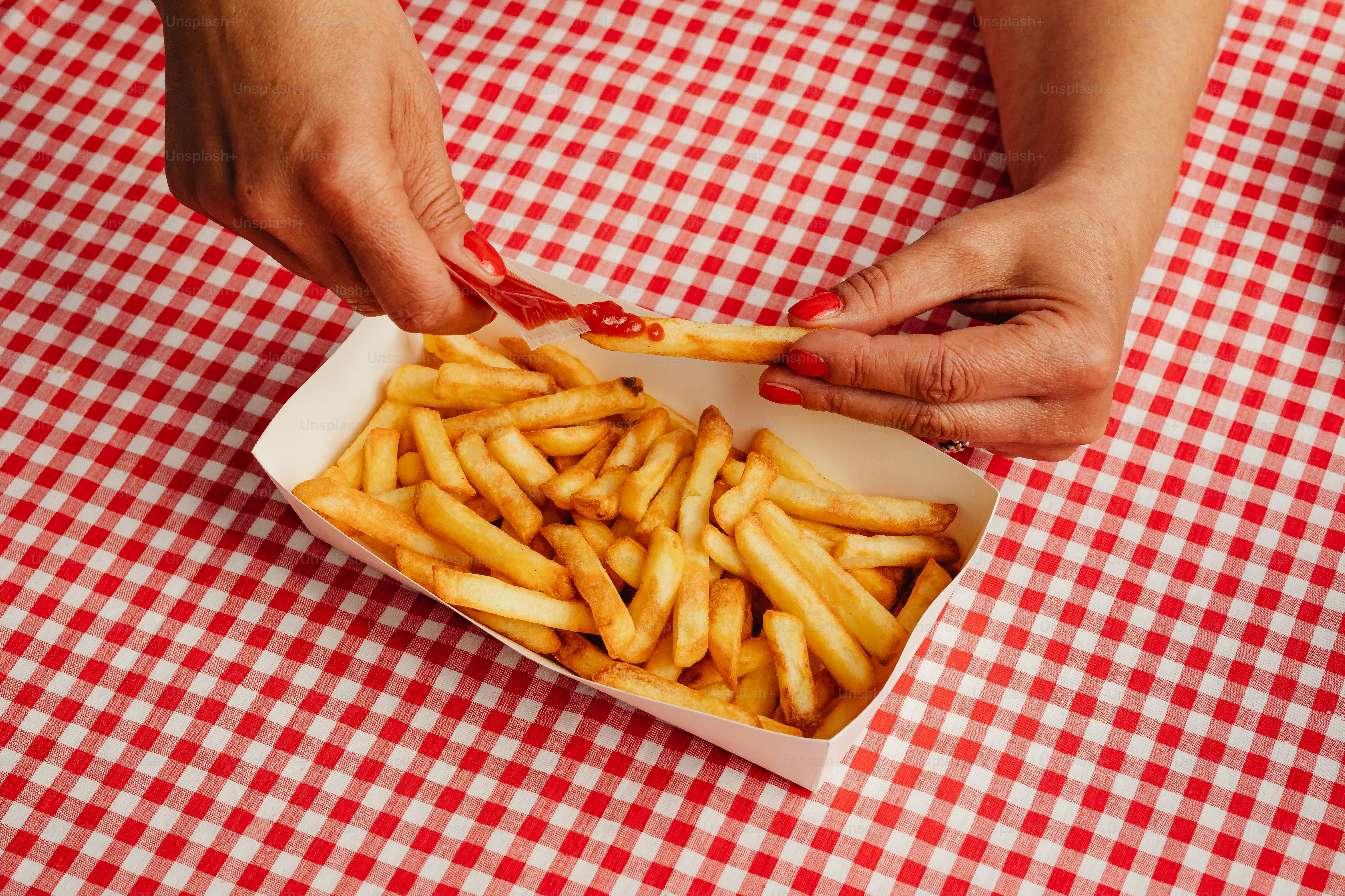 A person putting ketchup on french fries in a box photo Fast food