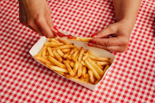 a person putting ketchup on french fries in a box