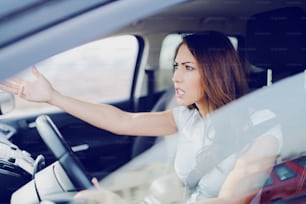 Morena caucasiana atraente irritada gritando com outros motoristas enquanto estava sentada no carro.