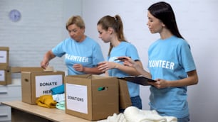 Voluntarios poniendo ropa en cajas de donaciones, trabajador social haciendo notas de caridad