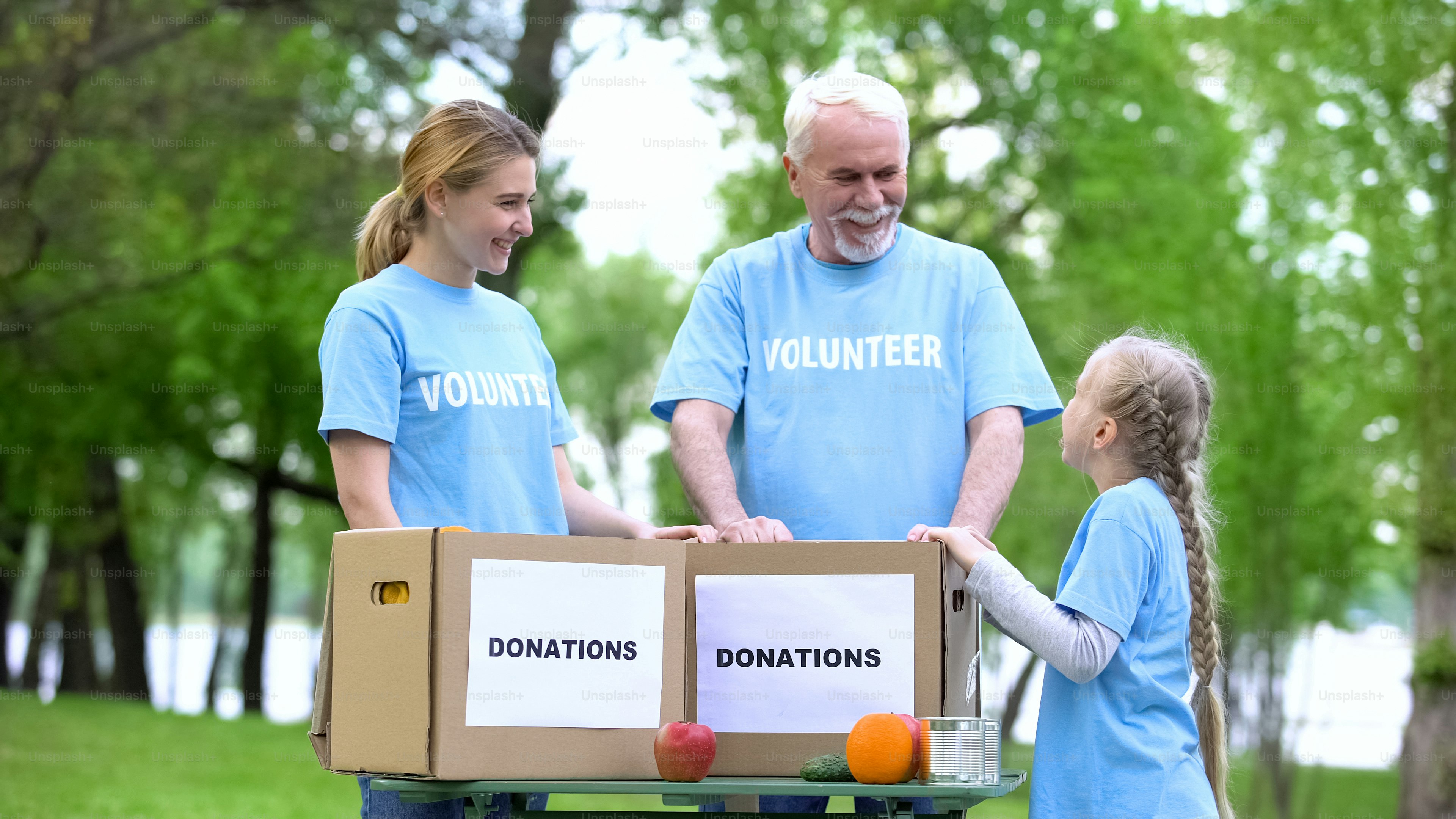 Child volunteer talking to family, fruits and canned food with donation boxes
