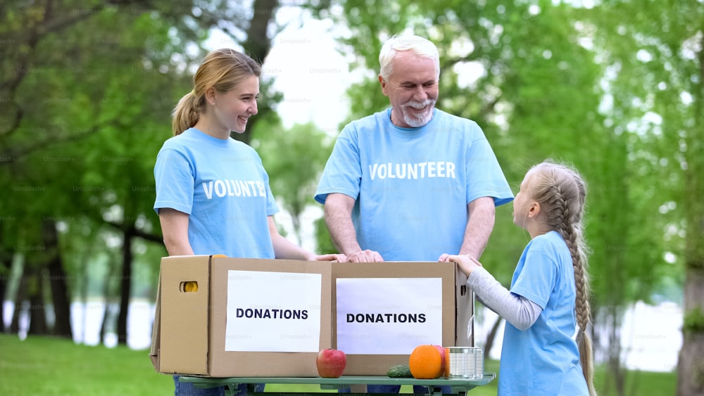 Child volunteer talking to family, fruits and canned food with donation boxes