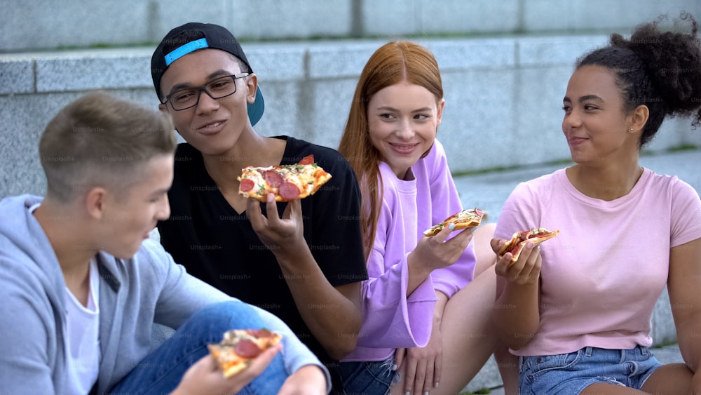 Joyful young people enjoying time together eating pizza outdoors, friendship