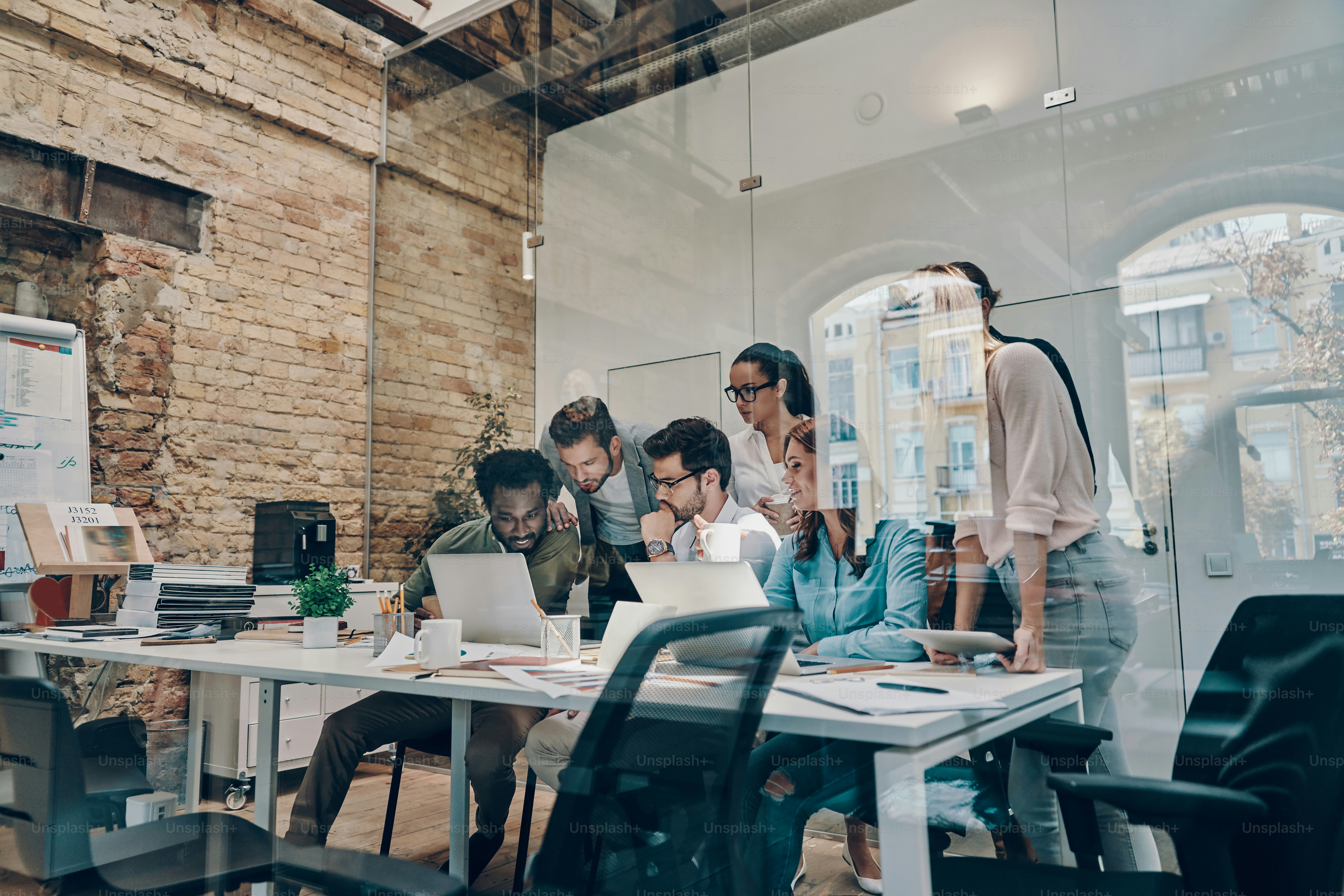 Group of young modern people in smart casual wear communicating and using modern technologies while working in the office