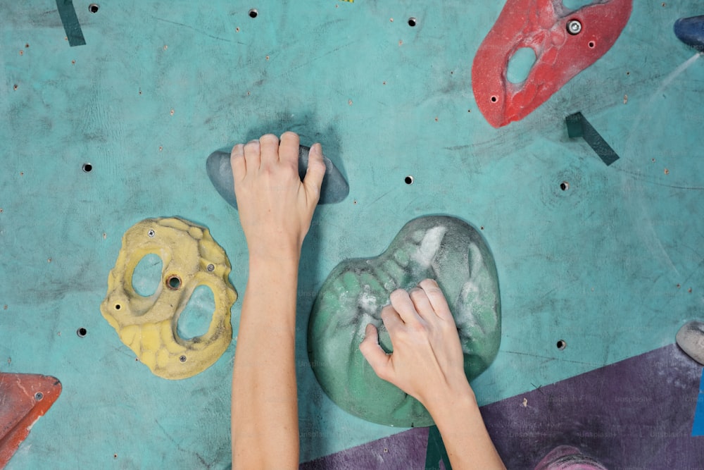 Hands of young sportswoman grabbing by artificial rocks while reaching for upper point of climbing equipment during training