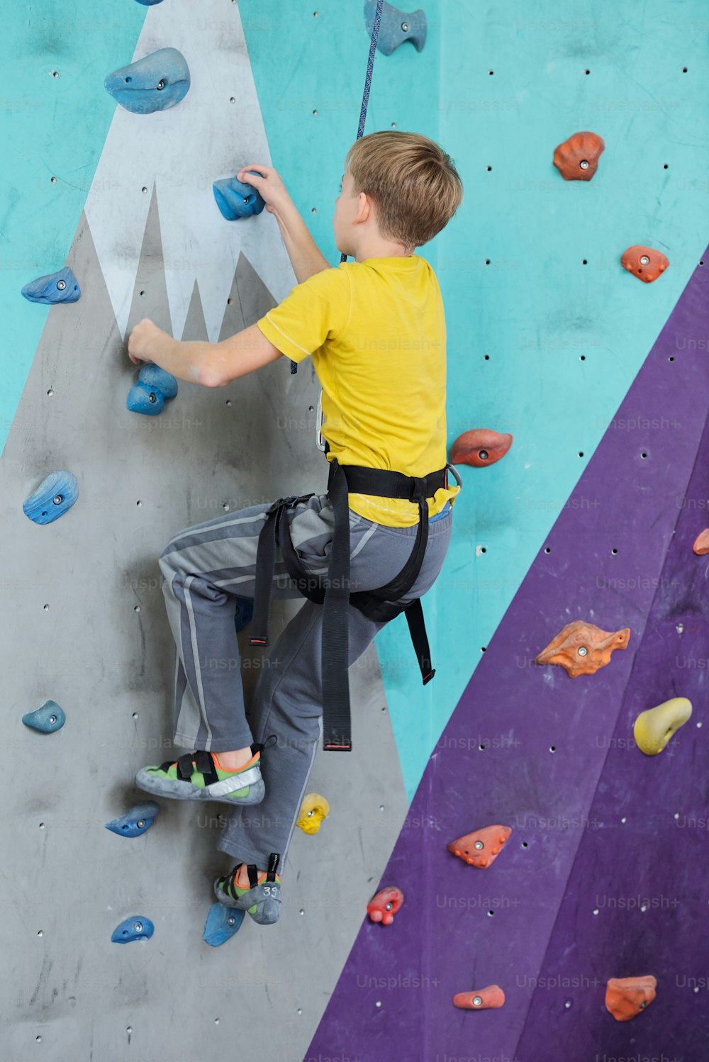 Side view of youthful boy in activewear climbing wall while grabbing by small rocks during indoor training