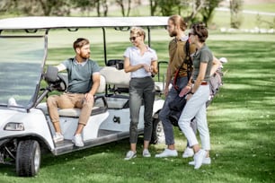 Group of a young friends hanging out together with golf equipment near the golf car on the playing course before the game