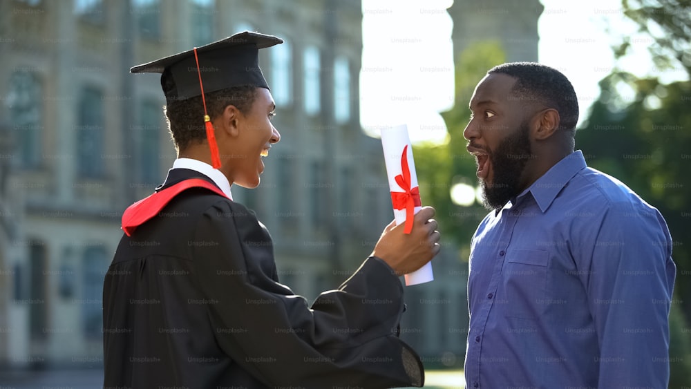 Excited dad rejoicing graduating son with diploma, study achievement, education
