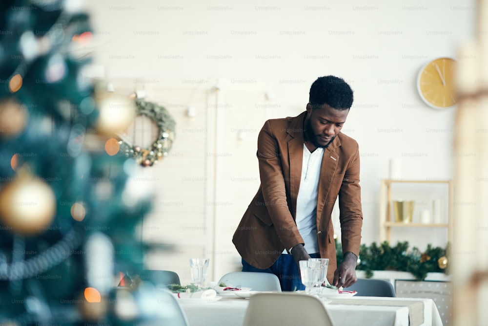 Portrait of modern African-American man decorating dining room for Christmas party, copy space
