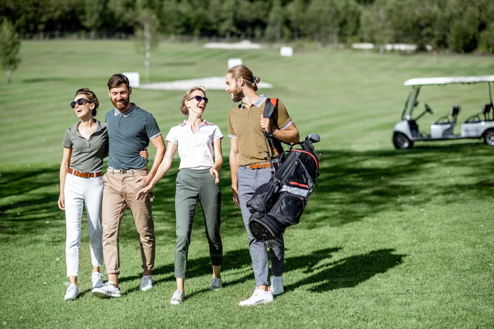 Young and elegant friends walking with golf equipment, hanging out together on the beautiful course with golf car on the background
