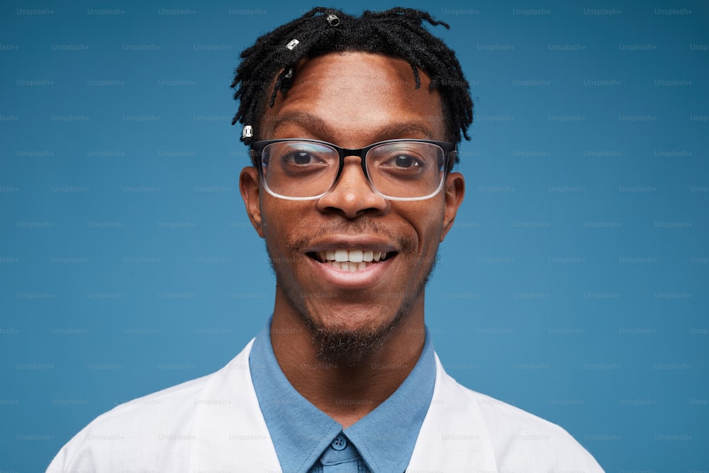 Head and shoulders portrait of contemporary African-American man smiling at camera while posing against blue background, copy space