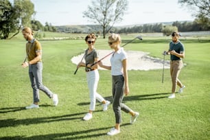 Giovani amici vestiti casualmente che camminano con putter sul campo da golf durante una partita in una giornata di sole
